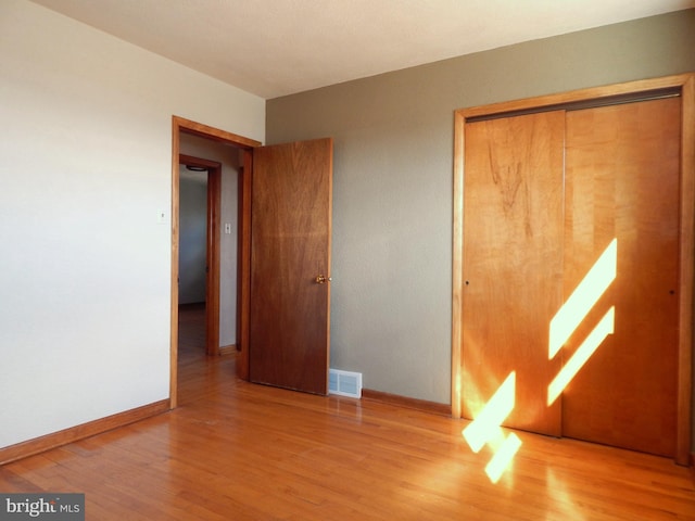 unfurnished bedroom with baseboards, a closet, visible vents, and wood finished floors