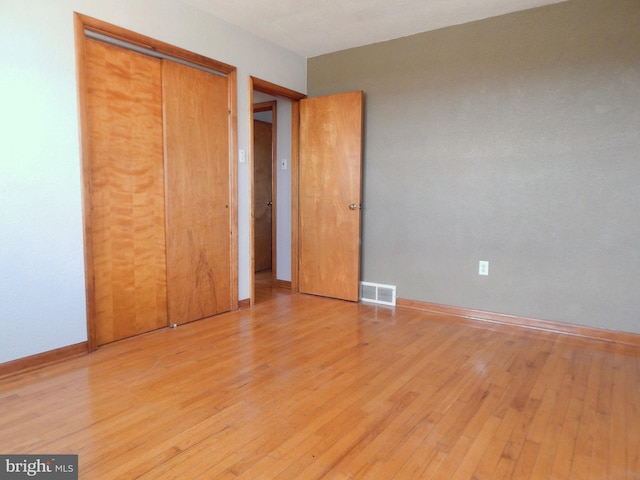 unfurnished bedroom featuring light wood-style flooring, a closet, visible vents, and baseboards