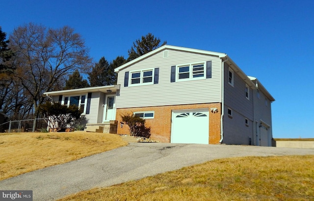 split level home with an attached garage, driveway, a front yard, and brick siding