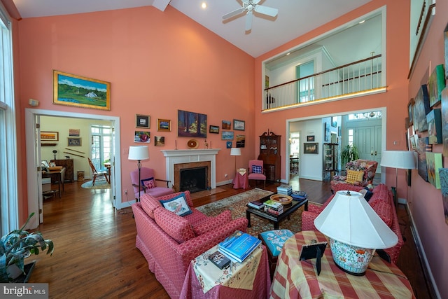 living room with a fireplace with flush hearth, a ceiling fan, wood finished floors, high vaulted ceiling, and baseboards