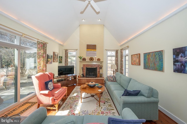 living area with ceiling fan, high vaulted ceiling, wood finished floors, baseboards, and a brick fireplace