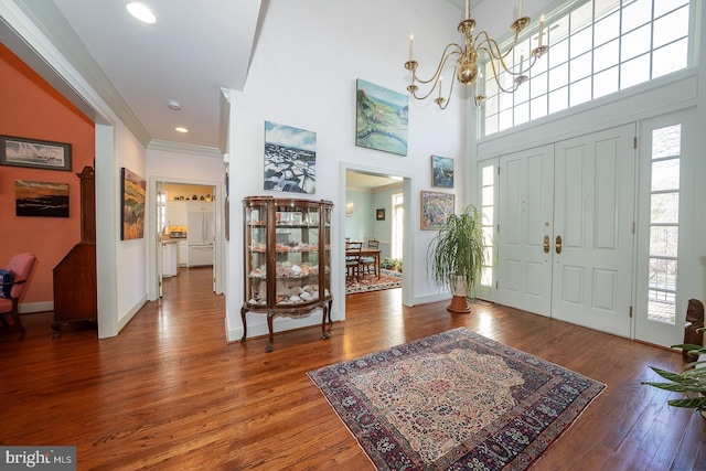 foyer entrance featuring a chandelier, a high ceiling, wood finished floors, baseboards, and ornamental molding