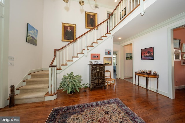 staircase featuring baseboards, wood finished floors, a towering ceiling, and crown molding