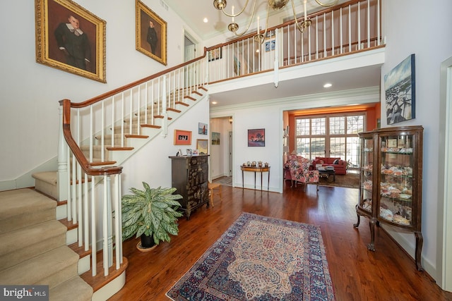 foyer with a towering ceiling, ornamental molding, and wood finished floors