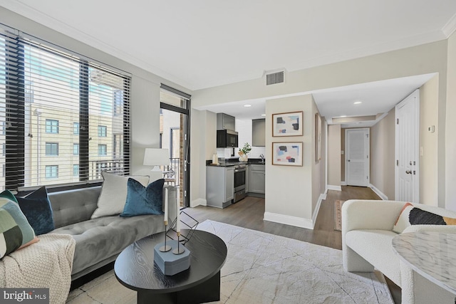 living area with baseboards, visible vents, wood finished floors, and ornamental molding