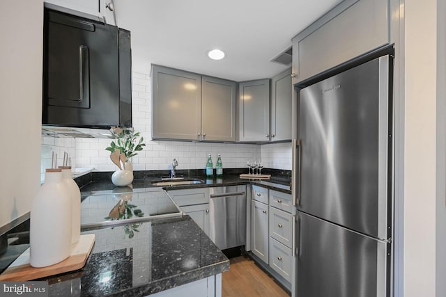 kitchen with appliances with stainless steel finishes, wood finished floors, gray cabinets, and tasteful backsplash