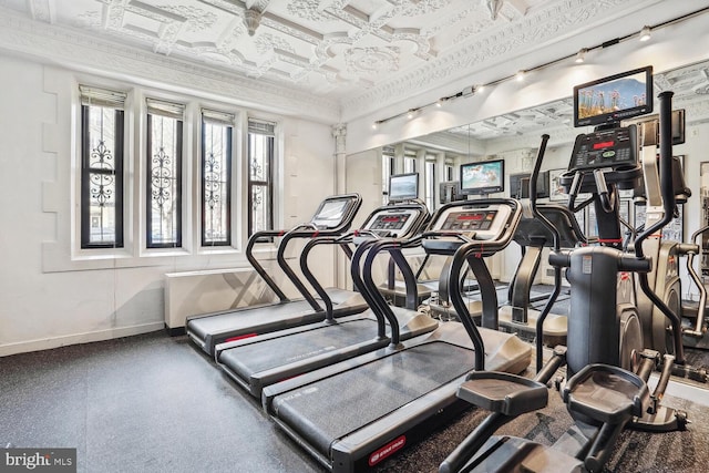 exercise room with an ornate ceiling, track lighting, baseboards, and crown molding