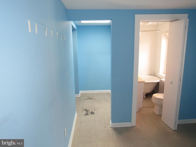 interior space with radiator, a soaking tub, baseboards, and toilet