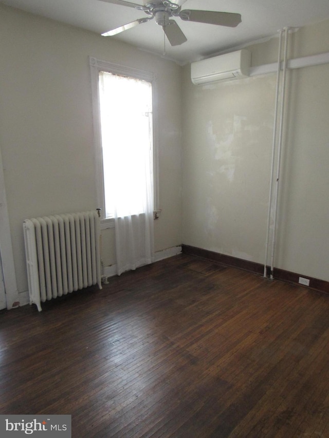 spare room featuring a wall unit AC, radiator heating unit, baseboards, and dark wood-type flooring