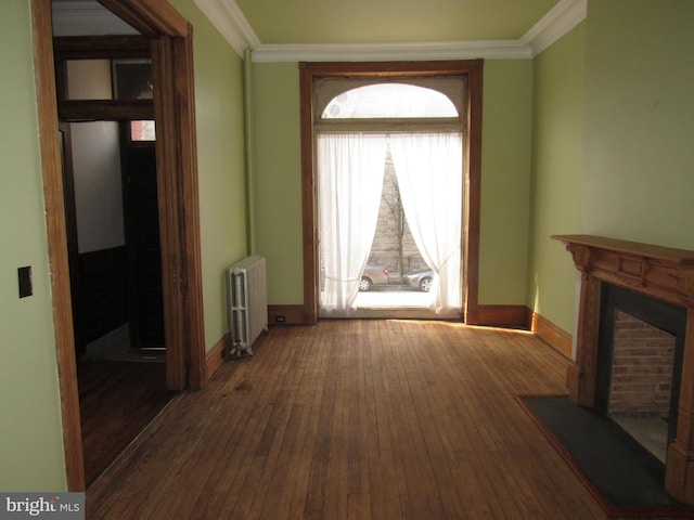 hallway featuring baseboards, hardwood / wood-style floors, radiator heating unit, and crown molding