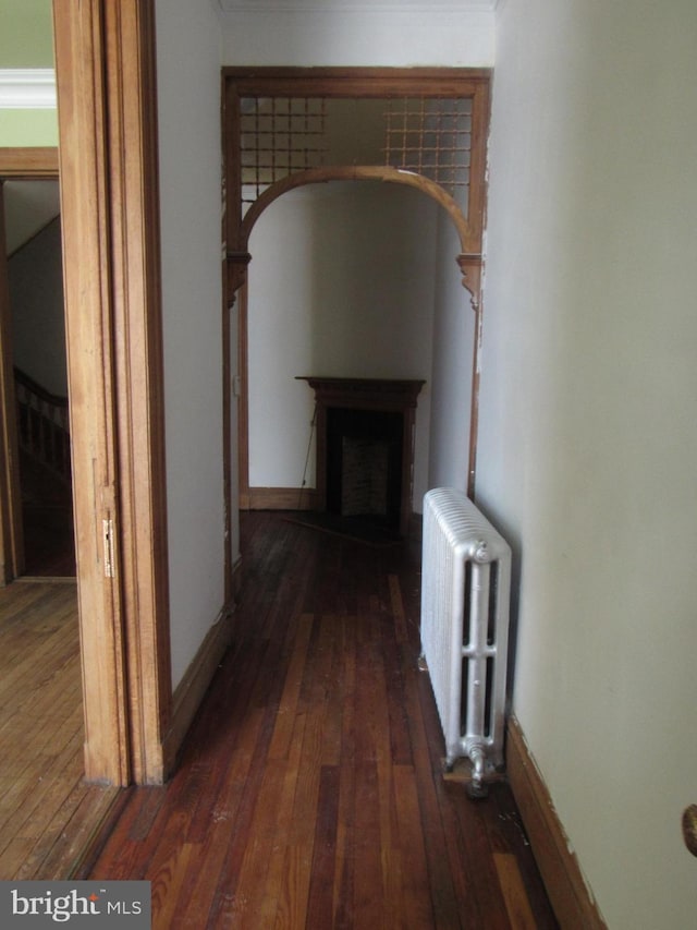 hallway with hardwood / wood-style flooring, radiator heating unit, baseboards, and arched walkways