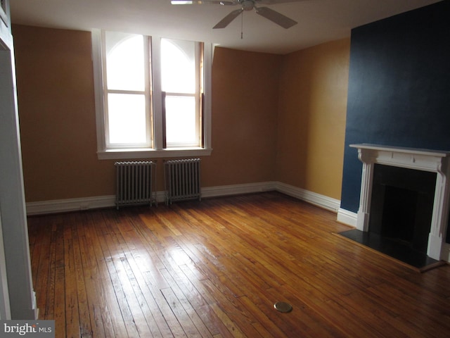 unfurnished living room featuring baseboards, radiator heating unit, ceiling fan, hardwood / wood-style floors, and a fireplace