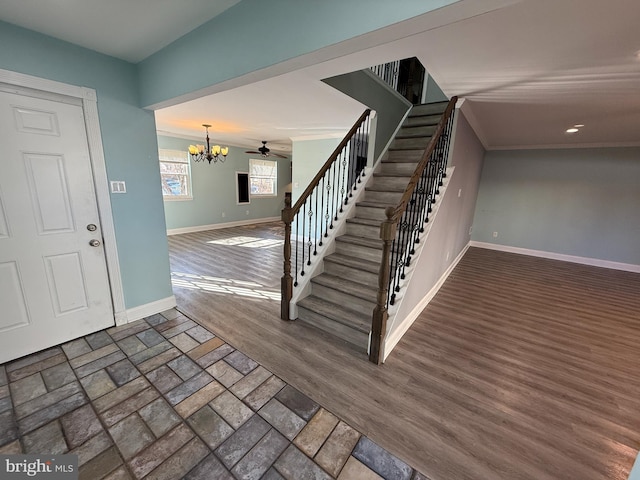 staircase with crown molding, ceiling fan with notable chandelier, wood finished floors, and baseboards