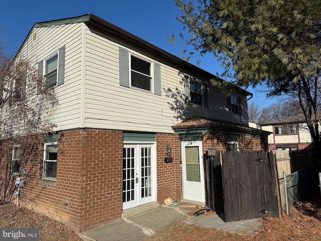 view of front facade with brick siding, fence, and french doors