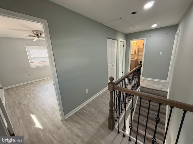 corridor featuring attic access, baseboards, light wood-style flooring, and an upstairs landing