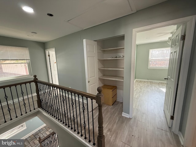 hall with light wood finished floors, attic access, baseboards, and an upstairs landing