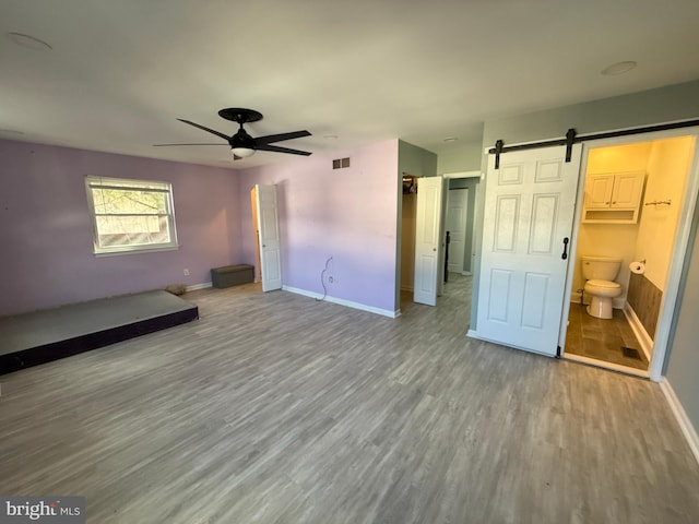 unfurnished bedroom with visible vents, a barn door, ceiling fan, wood finished floors, and baseboards