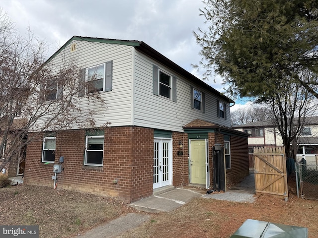 exterior space featuring french doors, brick siding, fence, and a gate