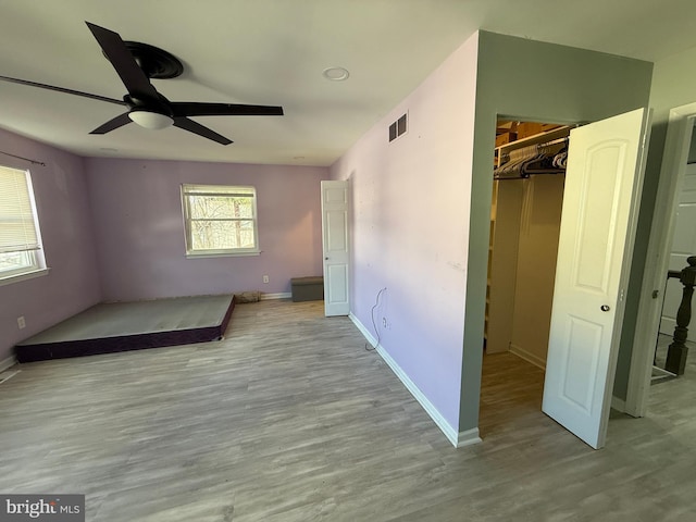 unfurnished bedroom with a walk in closet, visible vents, a ceiling fan, wood finished floors, and baseboards