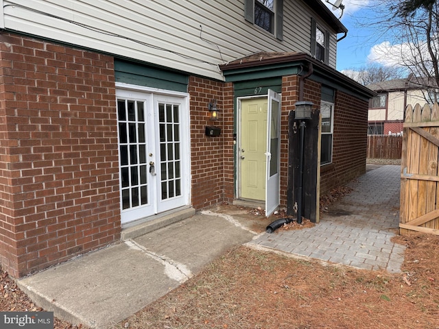 property entrance featuring brick siding, fence, and french doors