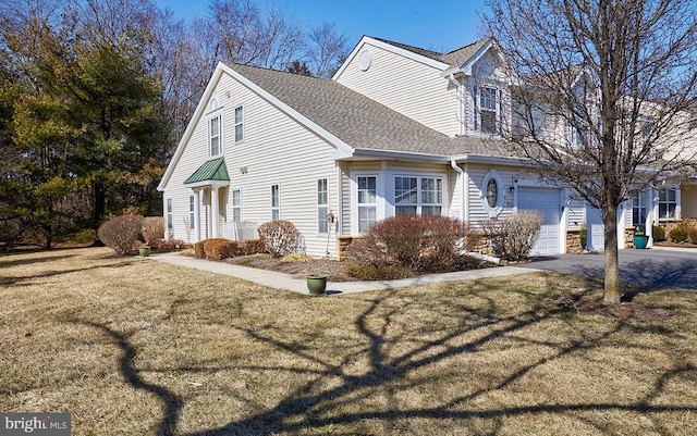 view of side of property with a garage, driveway, a lawn, and roof with shingles