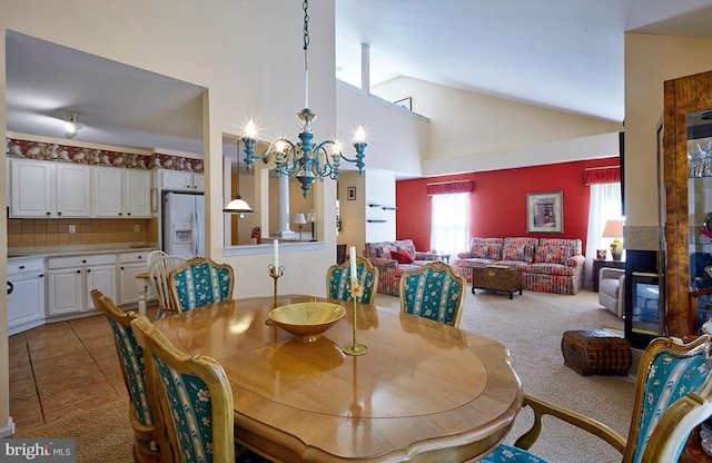 dining area with an inviting chandelier, light tile patterned floors, high vaulted ceiling, and light colored carpet