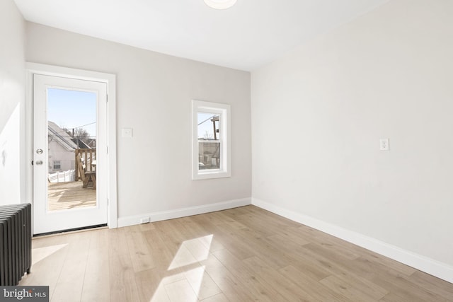 empty room with light wood-type flooring, radiator, and baseboards