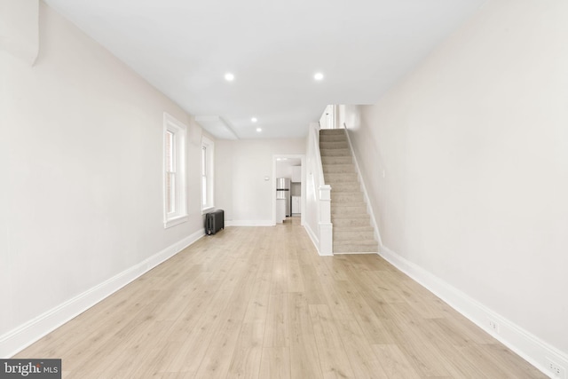 unfurnished living room with recessed lighting, radiator, light wood-style flooring, stairway, and baseboards