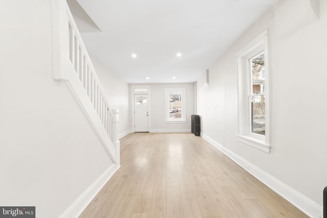 foyer entrance with light wood-type flooring, radiator, baseboards, and stairs