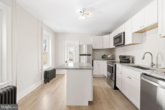 kitchen featuring appliances with stainless steel finishes, a sink, light stone countertops, and radiator