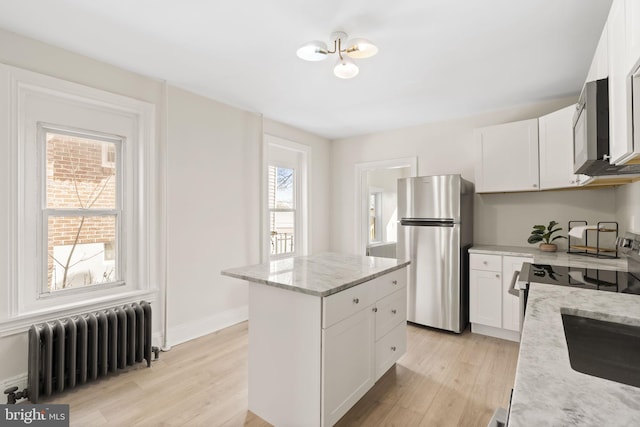 kitchen with a center island, light wood finished floors, radiator, appliances with stainless steel finishes, and white cabinetry