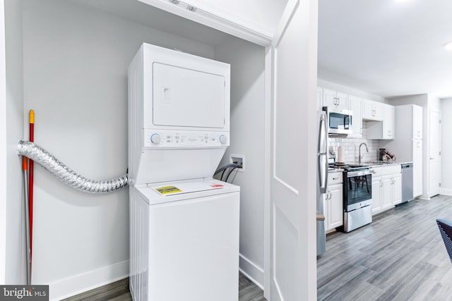 clothes washing area featuring light wood-style flooring, stacked washer / dryer, a sink, laundry area, and baseboards