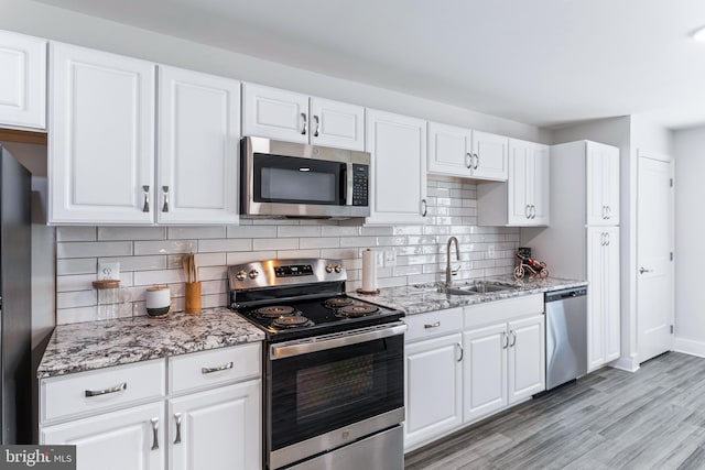 kitchen with stainless steel appliances, white cabinets, a sink, and backsplash