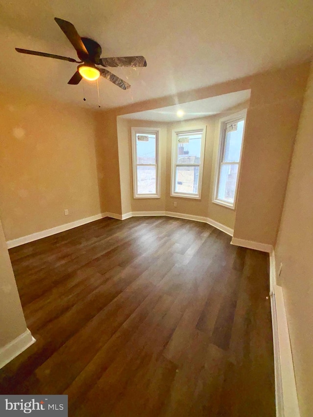 empty room with a ceiling fan, baseboards, and dark wood-style flooring