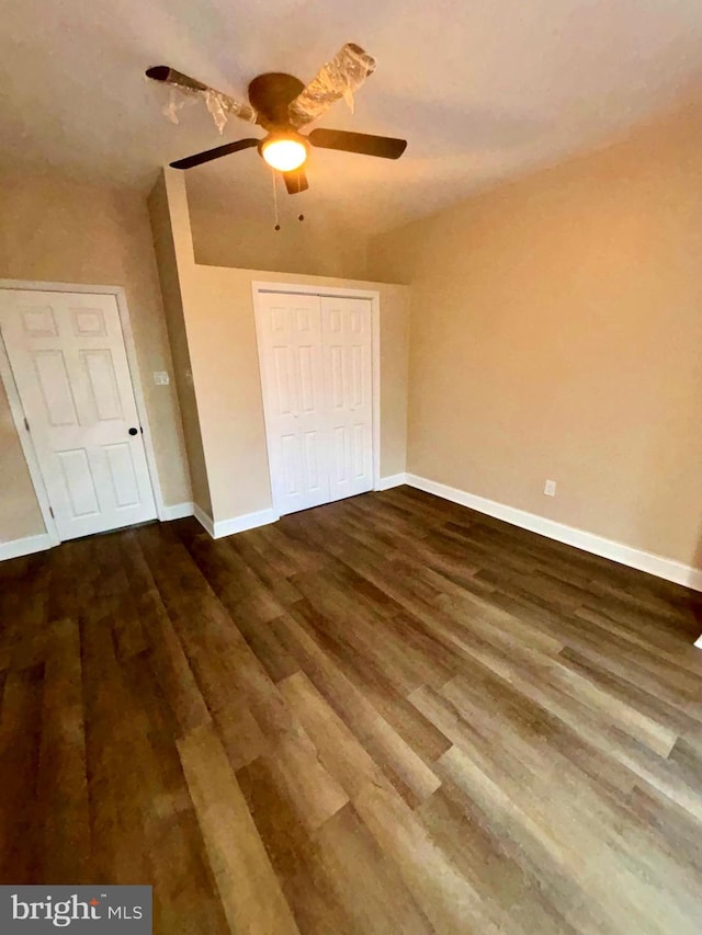 unfurnished bedroom with dark wood-style floors, baseboards, and a closet