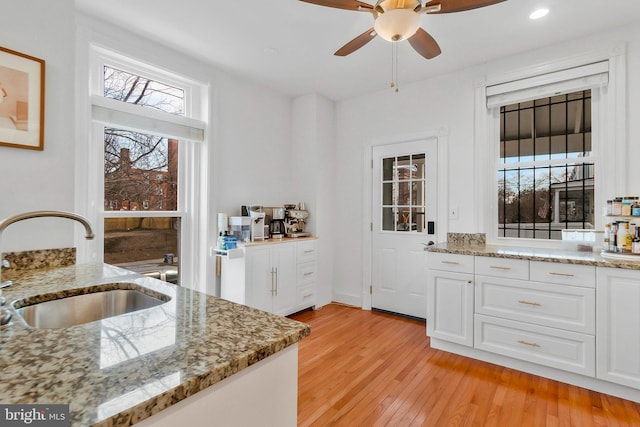 kitchen with light stone counters, a sink, light wood-style flooring, and white cabinets