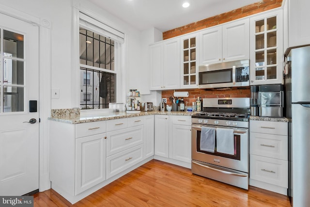 kitchen featuring glass insert cabinets, light wood finished floors, white cabinetry, and stainless steel appliances