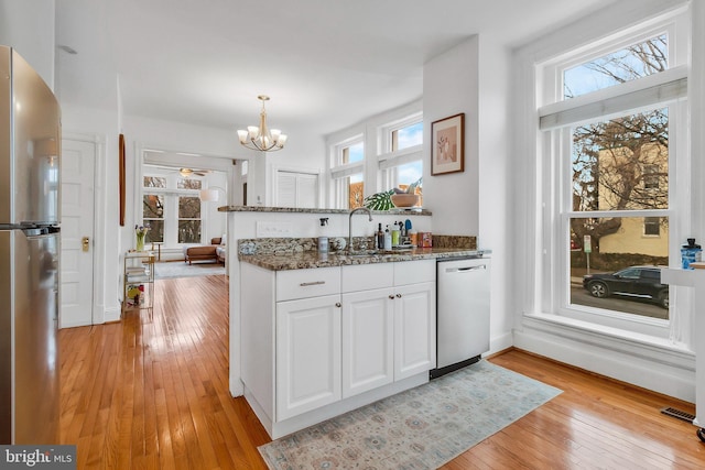 kitchen featuring light wood finished floors, appliances with stainless steel finishes, white cabinets, a sink, and a peninsula