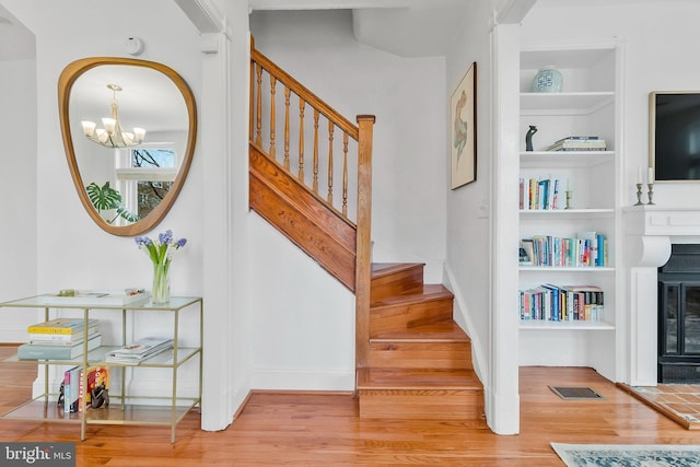 stairs featuring built in shelves, a glass covered fireplace, visible vents, and wood finished floors