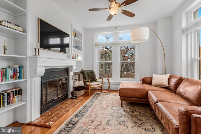 living area featuring a healthy amount of sunlight, built in features, wood finished floors, and a glass covered fireplace