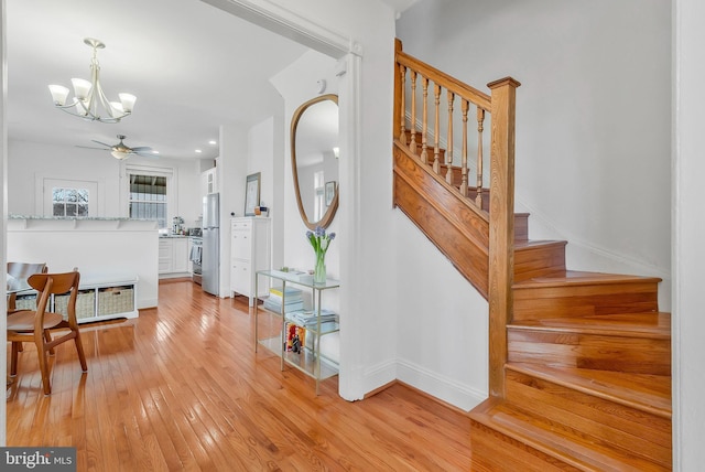 staircase featuring baseboards, hardwood / wood-style floors, and ceiling fan with notable chandelier