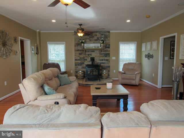 living room with baseboards, wood finished floors, ornamental molding, and a wood stove