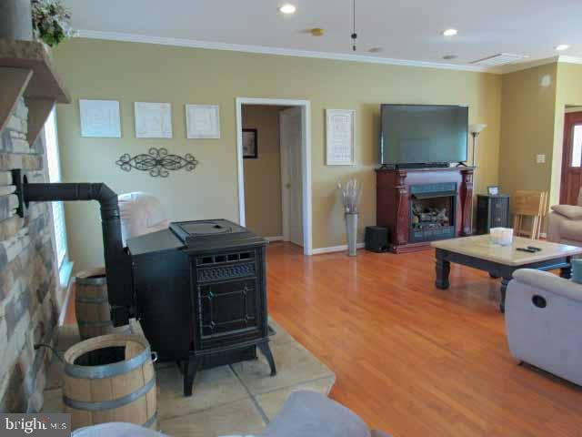 living room featuring crown molding, light wood-type flooring, recessed lighting, a fireplace, and a wood stove