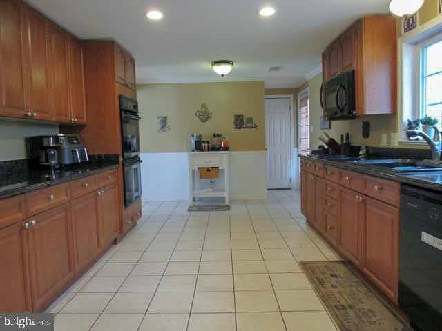 kitchen featuring light tile patterned floors, brown cabinets, dark countertops, and black appliances