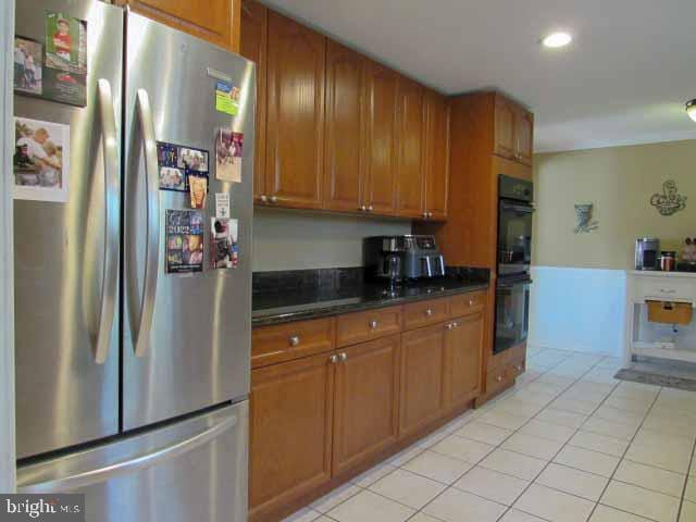 kitchen featuring light tile patterned floors, brown cabinetry, freestanding refrigerator, dobule oven black, and dark countertops