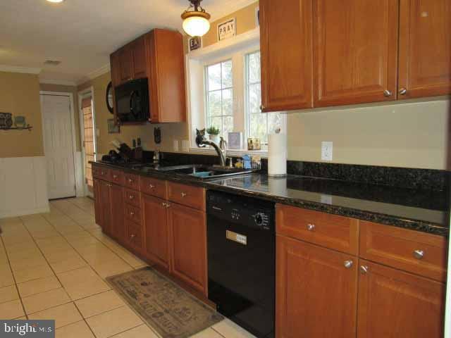 kitchen with black appliances, a sink, dark stone countertops, crown molding, and light tile patterned floors