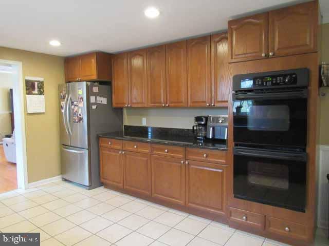 kitchen with dark countertops, recessed lighting, brown cabinets, freestanding refrigerator, and dobule oven black