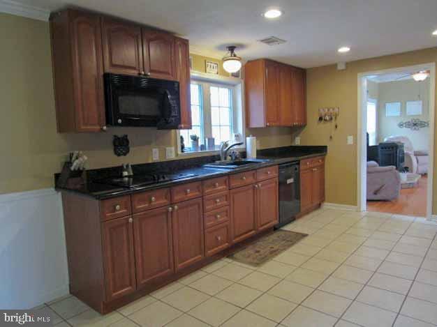 kitchen featuring visible vents, light tile patterned flooring, a sink, black appliances, and dark countertops