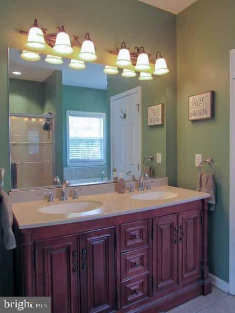 full bathroom with a sink, a shower with shower door, double vanity, and tile patterned floors