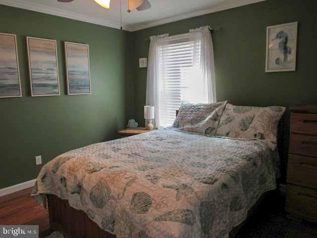 bedroom featuring ceiling fan, baseboards, wood finished floors, and crown molding